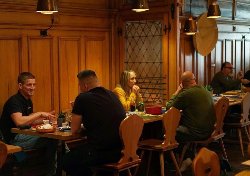 Eine Gruppe von Personen speist an einem Holztisch in einem Restaurant mit Pendelleuchten.