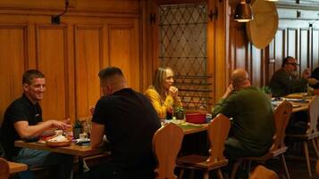 Eine Gruppe von Personen speist an einem Holztisch in einem Restaurant mit Pendelleuchten.