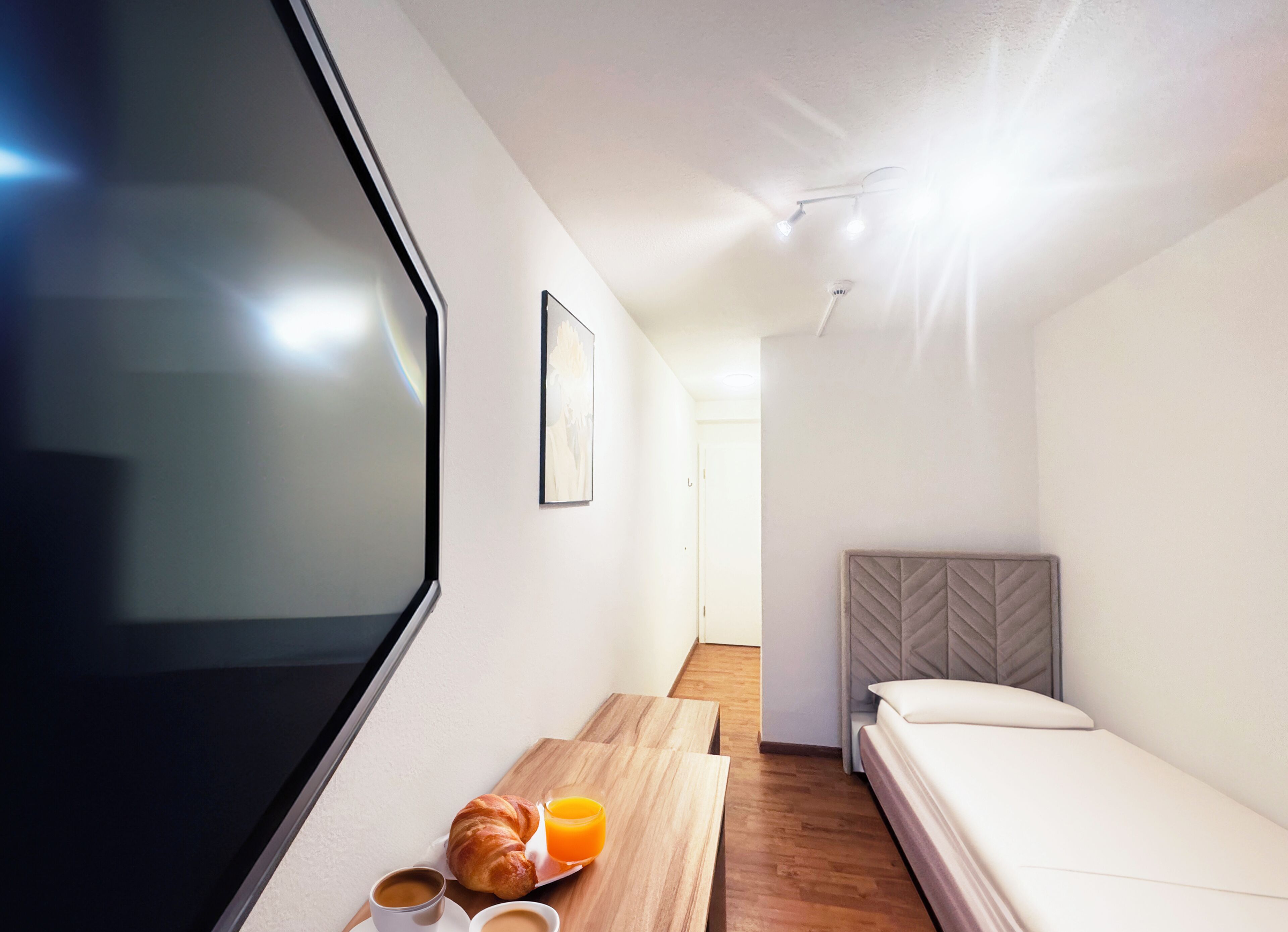 A modern hotel room with a large window, a wooden table with breakfast items, a bed, and a headboard.