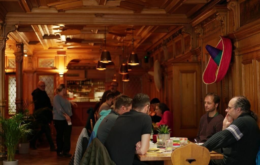 A restaurant interior with wooden paneling, hanging pendant lights, and a group of people dining.