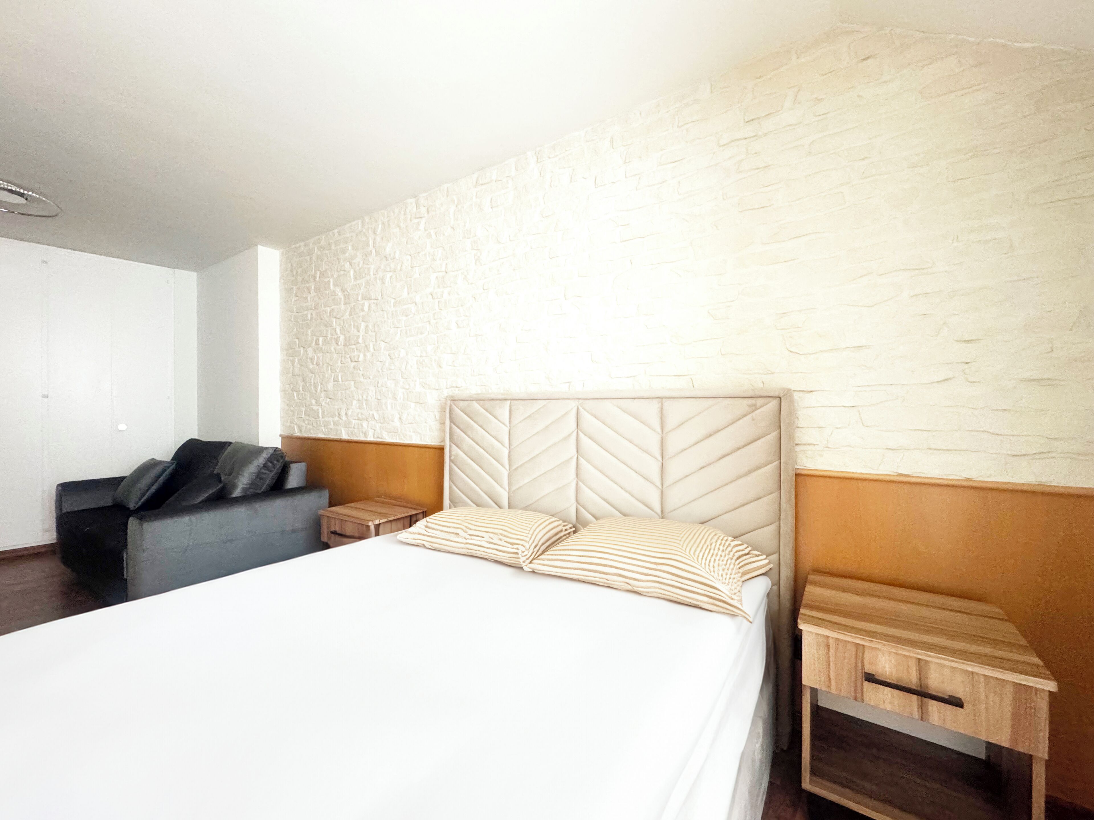 Une chambre d’hôtel avec un lit, un petit canapé, une table de chevet et une table d’appoint en bois.