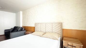 Une chambre d’hôtel avec un lit, un petit canapé, une table de chevet et une table d’appoint en bois.