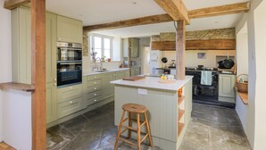 A kitchen with a central island, wooden beams, and a stone floor.