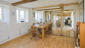 A spacious dining area with a wooden table and chairs, a kitchen in the background, and a large bookshelf.