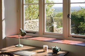 A room with a desk, a lamp, a mug, and a teapot. There is a window with a view of a stone wall and greenery. - Beautiful cottage set in peaceful surroundings with stunning views (Sand)