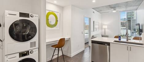 A modern laundry room with stacked washers and dryers, a small seating area, and a view of the city through a large window.