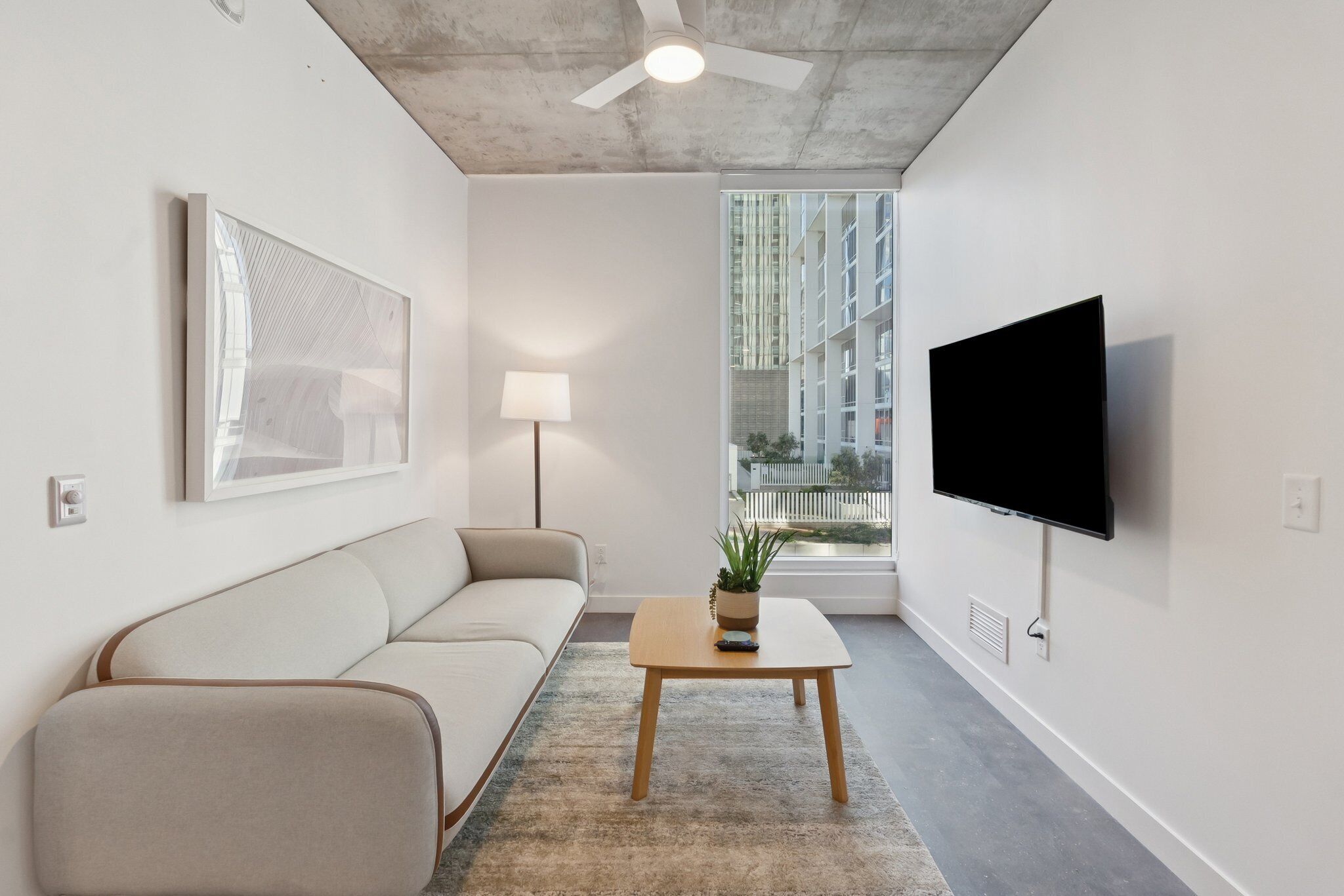 A modern living room with a sofa, a coffee table with a plant, a lamp, and a TV mounted on the wall.