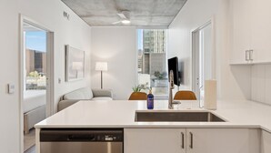 A modern kitchen with a dishwasher, a sink, and a dining area with a table and chairs. - Placemakr Downtown Phoenix (Phoenix)