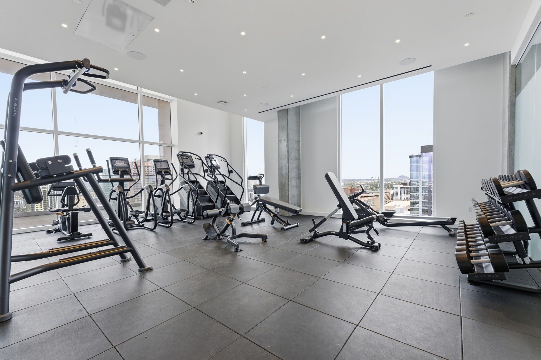 Une salle de sport moderne dotée de divers équipements d’entraînement, de grandes fenêtres et offrant une vue sur la ville.