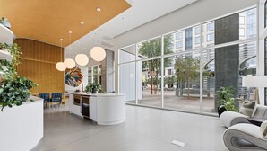 A modern reception area with a curved white counter, blue chairs, and a large window offering a view of the cityscape. - Placemakr Downtown Phoenix (Phoenix)