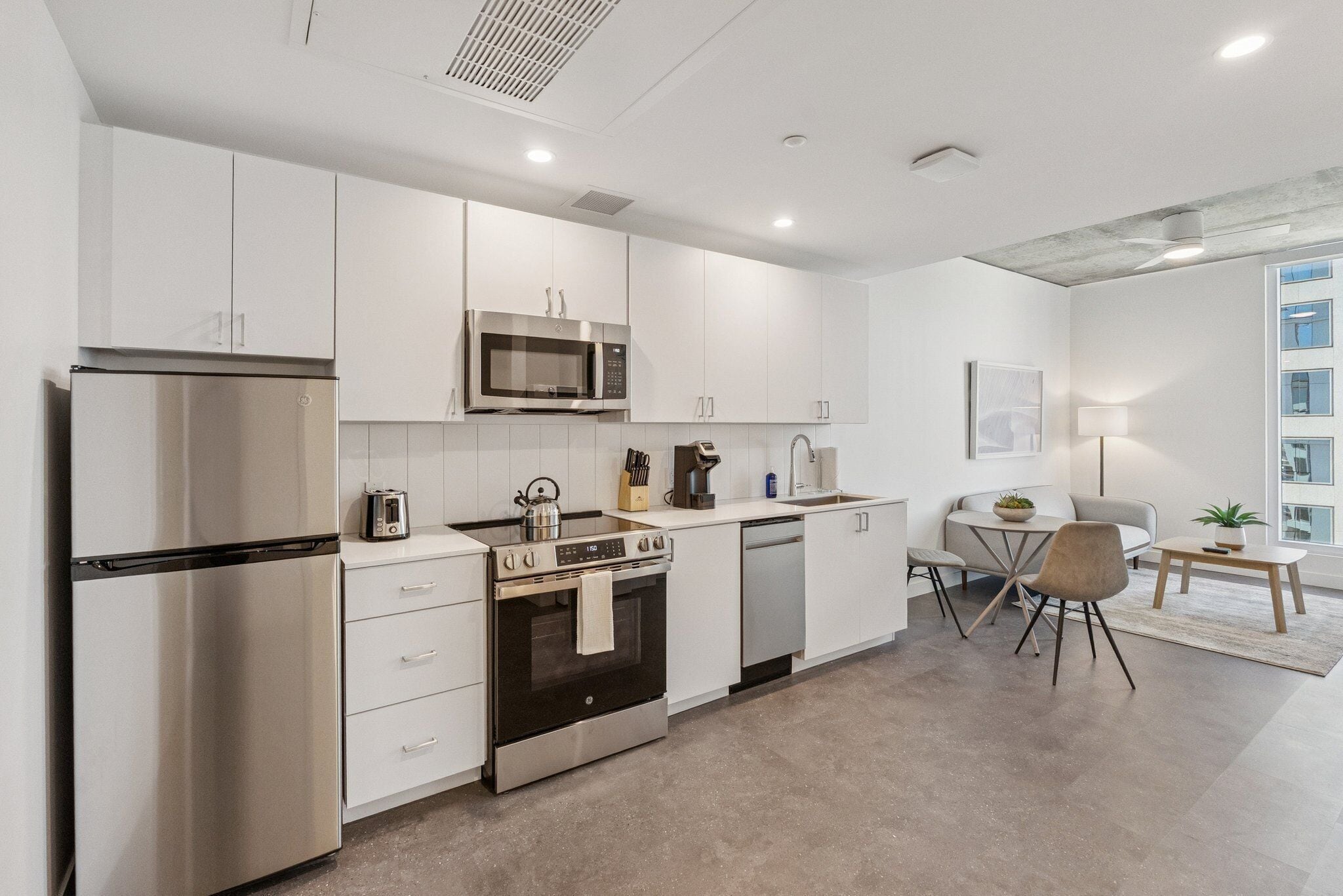 A modern kitchen with stainless steel appliances, white cabinetry, and a dining area with a table and chairs.