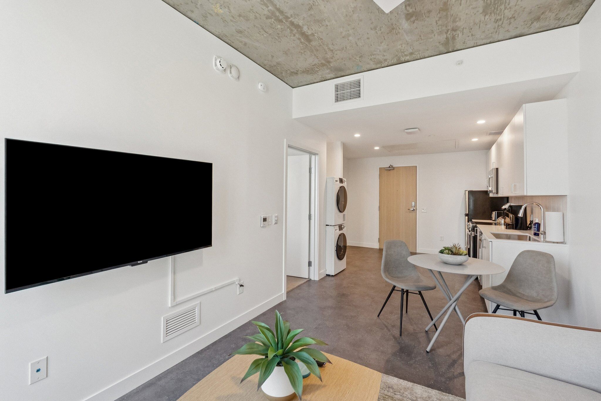 A modern living room with a flat-screen TV, a potted plant, and a dining area with two chairs and a small table.