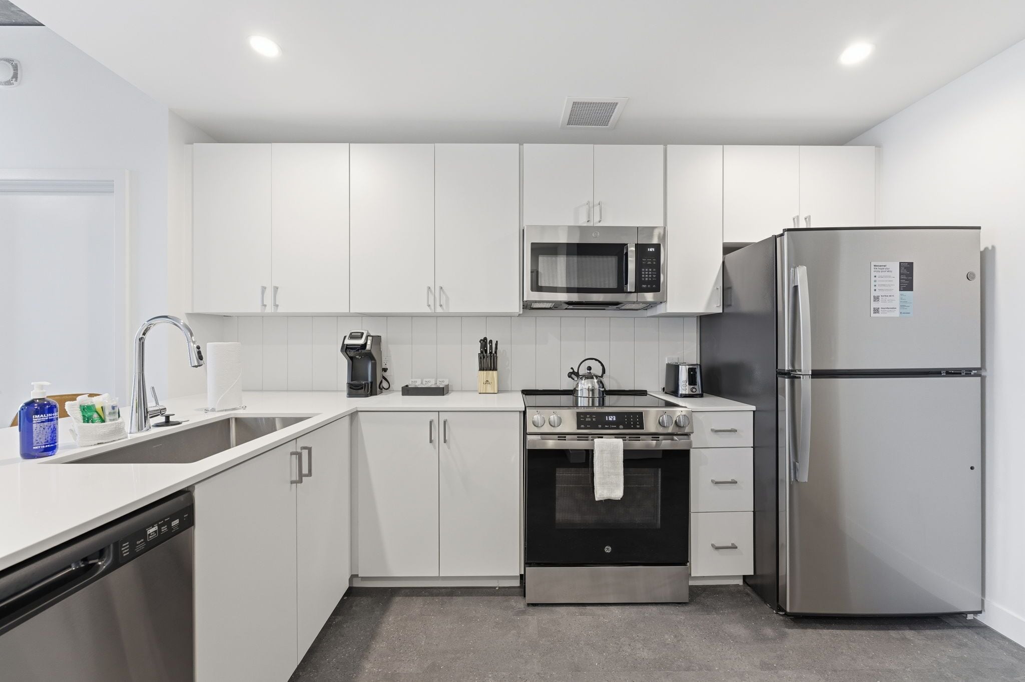 A modern kitchen with white cabinets, a stainless steel microwave, a refrigerator, a stove, and a dishwasher.