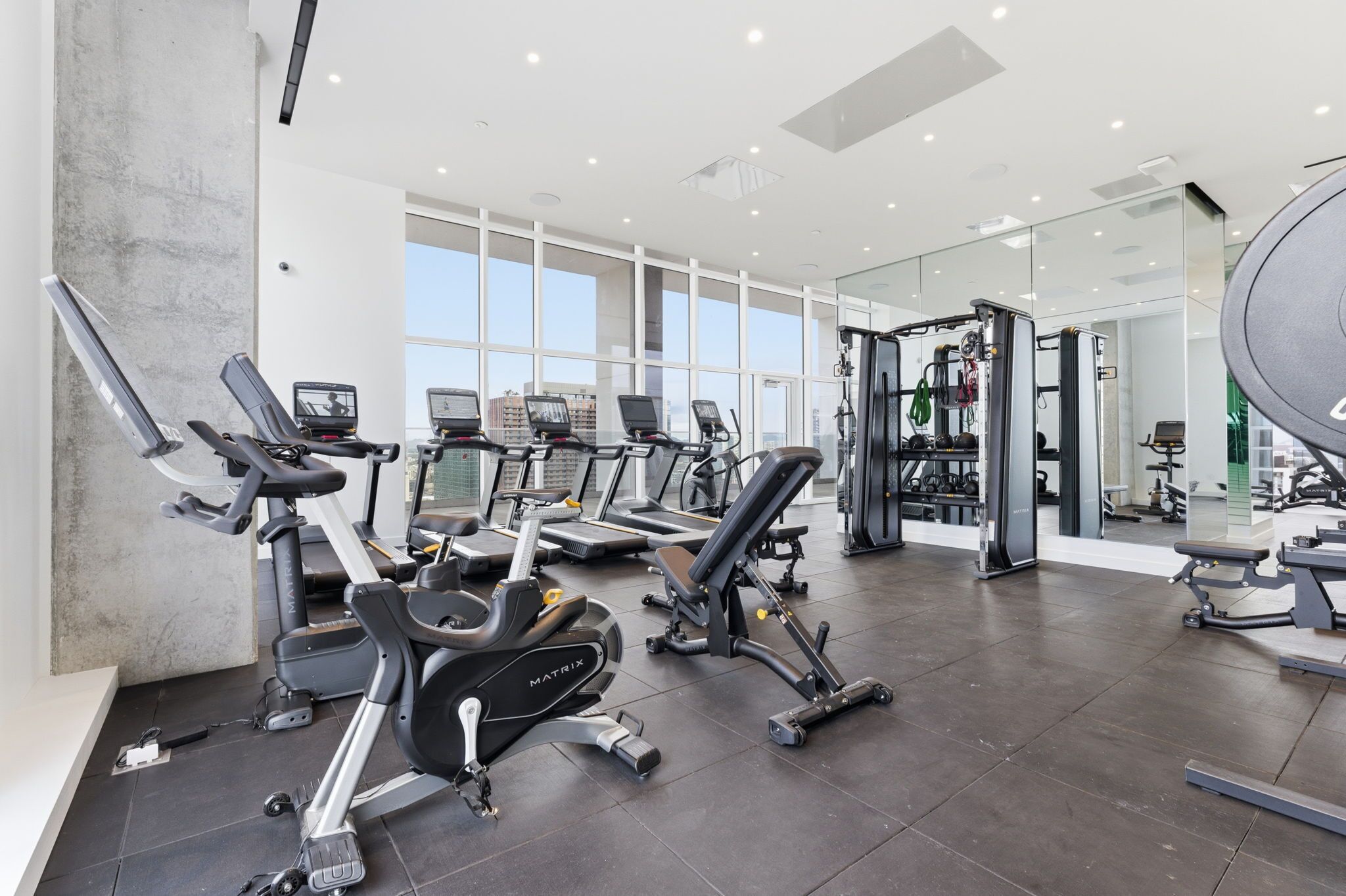 A modern gym with various exercise equipment, large windows, and a spacious layout.
