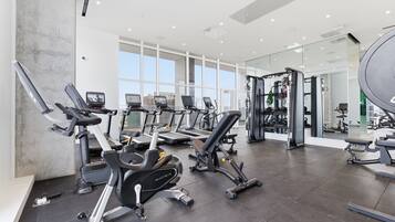 A modern gym with various exercise equipment, large windows, and a spacious layout.