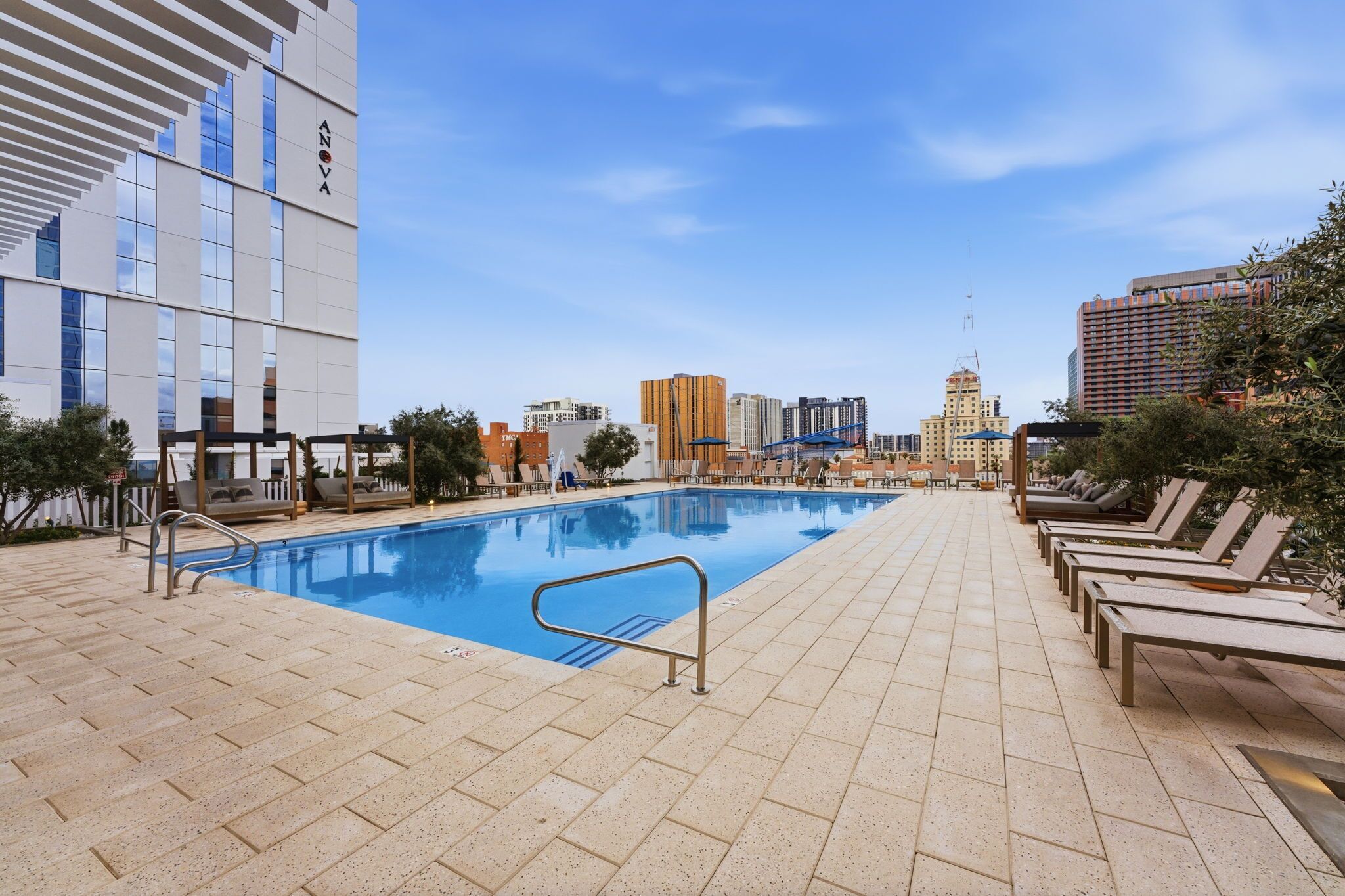 A rooftop pool area with lounge chairs, a pool, and a cityscape in the background.