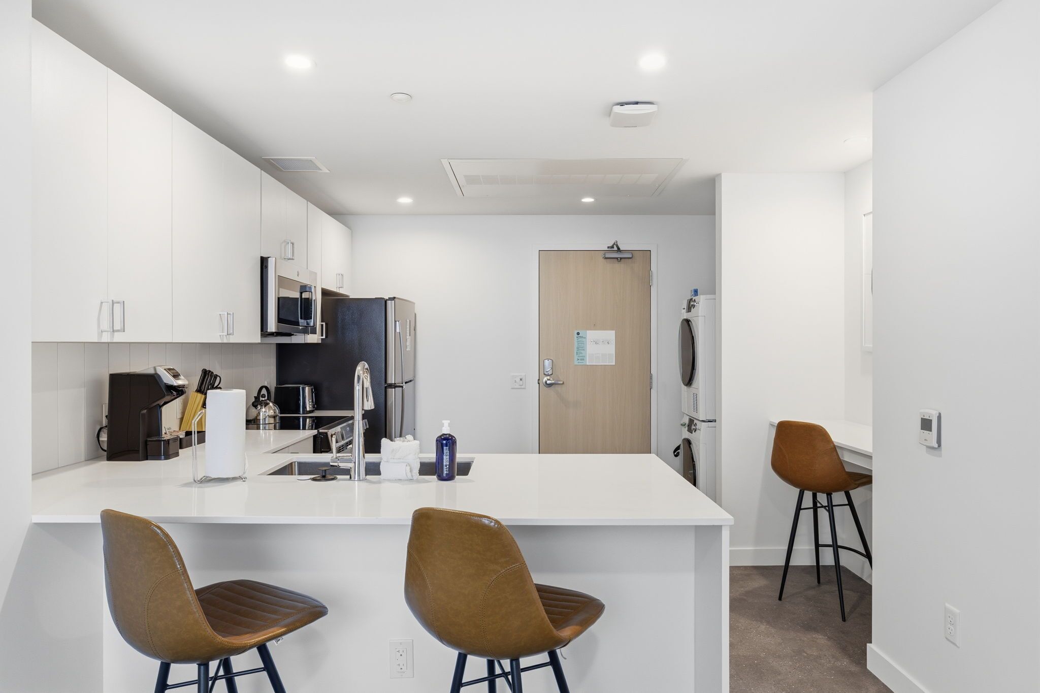 A modern kitchen with white cabinets, a microwave, a refrigerator, and two bar stools.