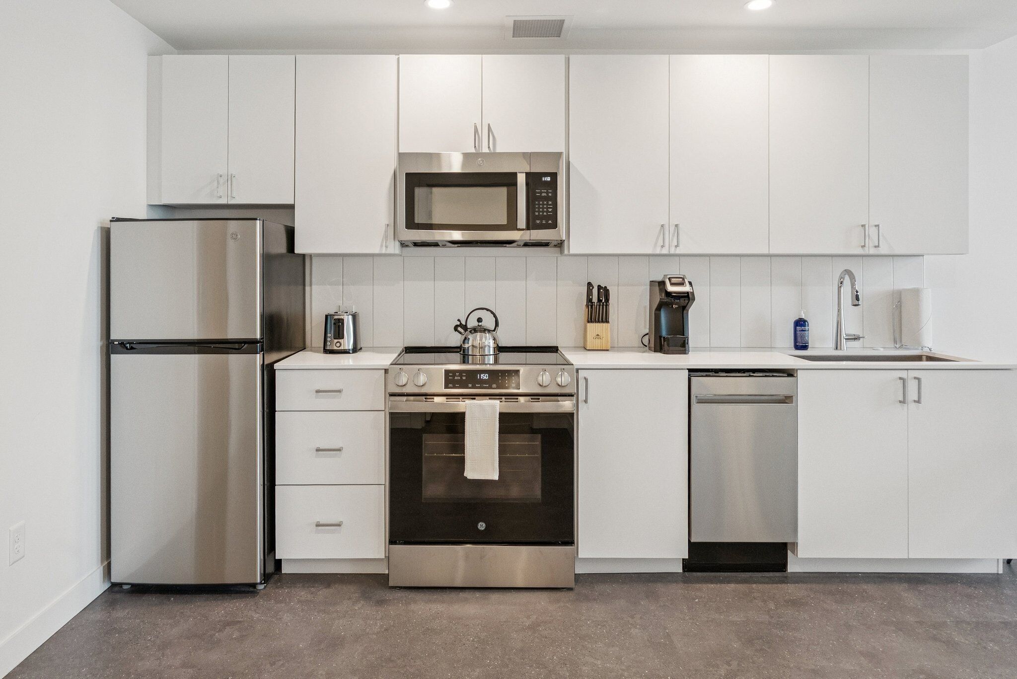 A modern kitchen with stainless steel appliances, white cabinetry, and a built-in oven.