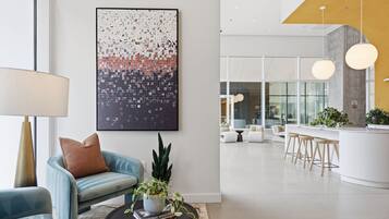 Un interior moderno con una zona de estar, una mesa de centro con libros y una planta, y un cuadro abstracto grande en la pared.