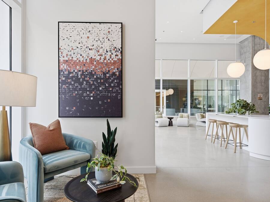 Un interior moderno con una zona de estar, una mesa de centro con libros y una planta, y un cuadro abstracto grande en la pared.