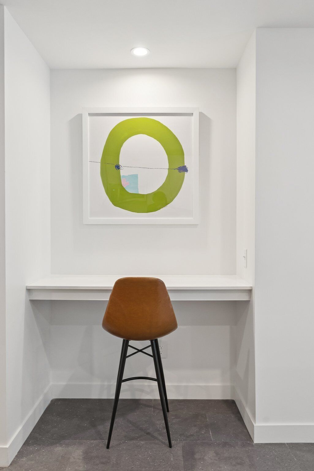 A modern room with a white desk, a brown chair, and a framed abstract art piece on the wall.