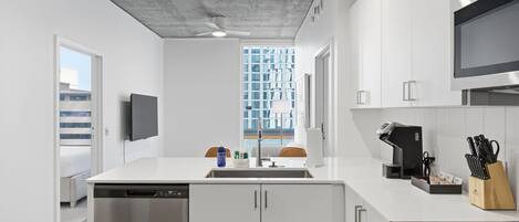 Eine moderne Küche mit weißen Schränken, einem eingebauten Backofen und einem großen Fenster mit Blick auf Gebäude.