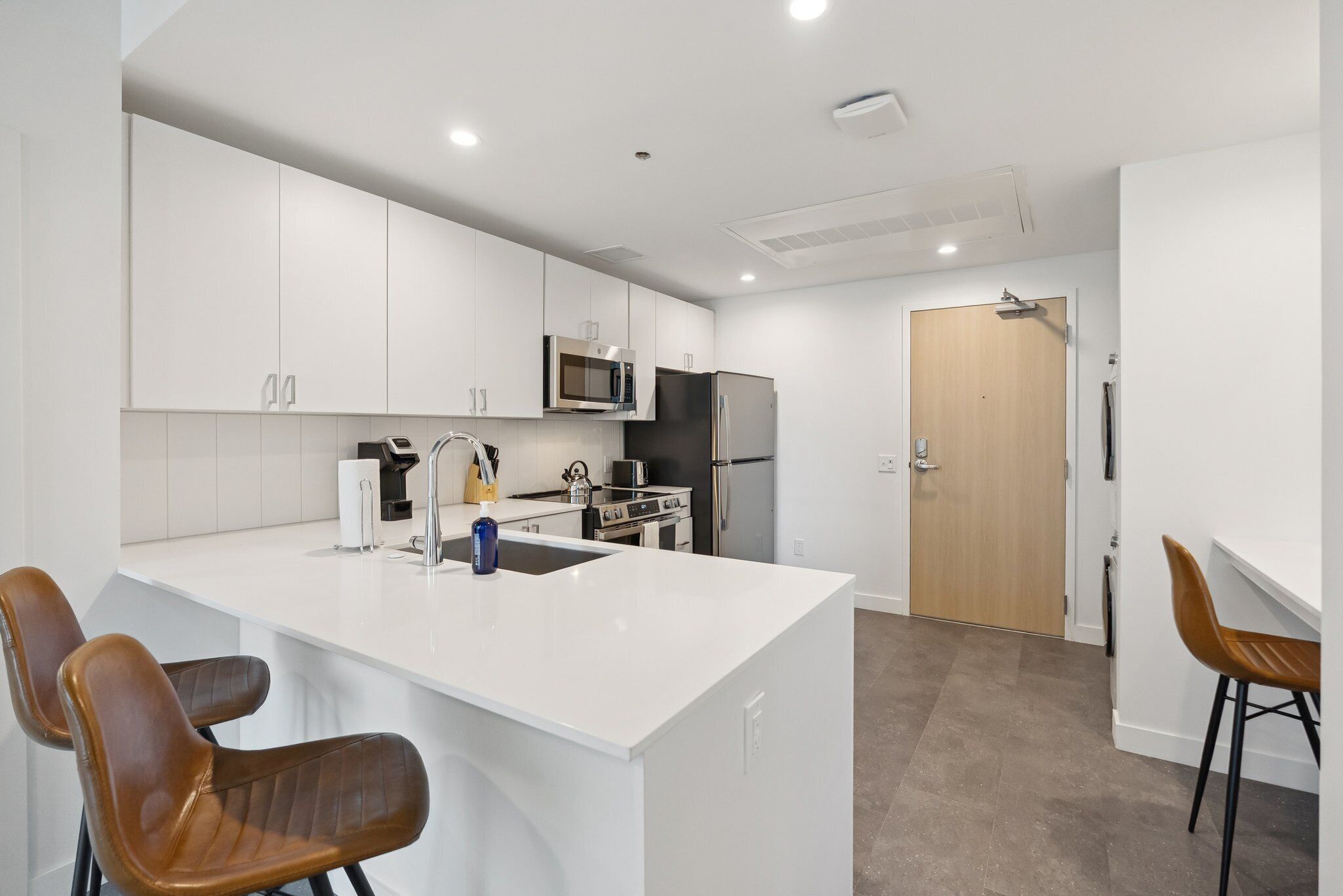 A modern kitchen with white cabinetry, a central island with seating, a microwave, a refrigerator, and a stove.