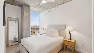 Una habitación de hotel moderna con una cama grande, dos lámparas de noche, un ventilador de techo y vistas a la ciudad.
