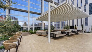 A modern outdoor seating area with wicker chairs and sofas, a pergola, and a view of the cityscape through large windows. - Placemakr Downtown Phoenix (Phoenix)