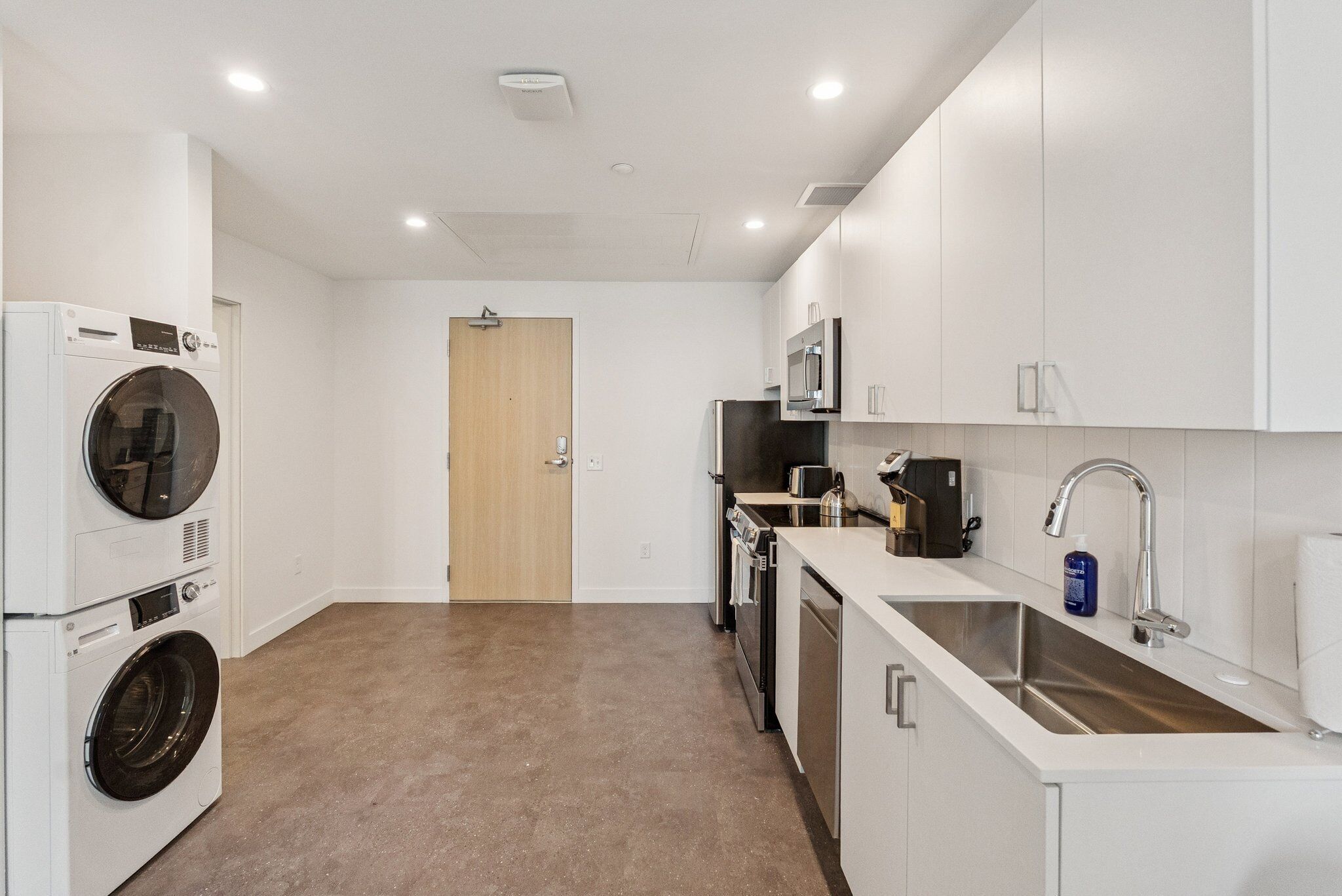A compact kitchen with a built-in washer and dryer, a microwave, a sink, and a door leading to another room.
