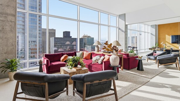 A modern living room with large windows, a red sofa, black chairs, and a small table with plants. - Placemakr Downtown Phoenix (Phoenix)