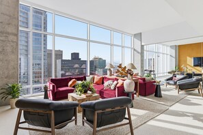 A modern living room with large windows, a red sofa, black chairs, and a small table with plants. - Placemakr Downtown Phoenix (Phoenix)