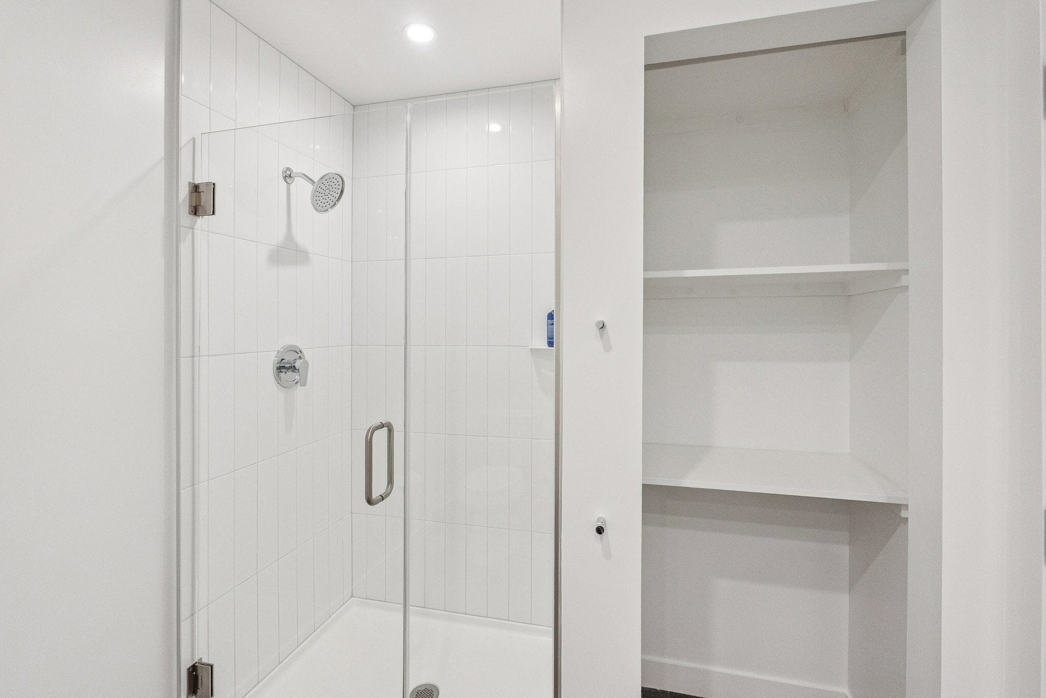 A modern bathroom with white tiled walls, a glass shower enclosure, a handheld showerhead, and a toilet.