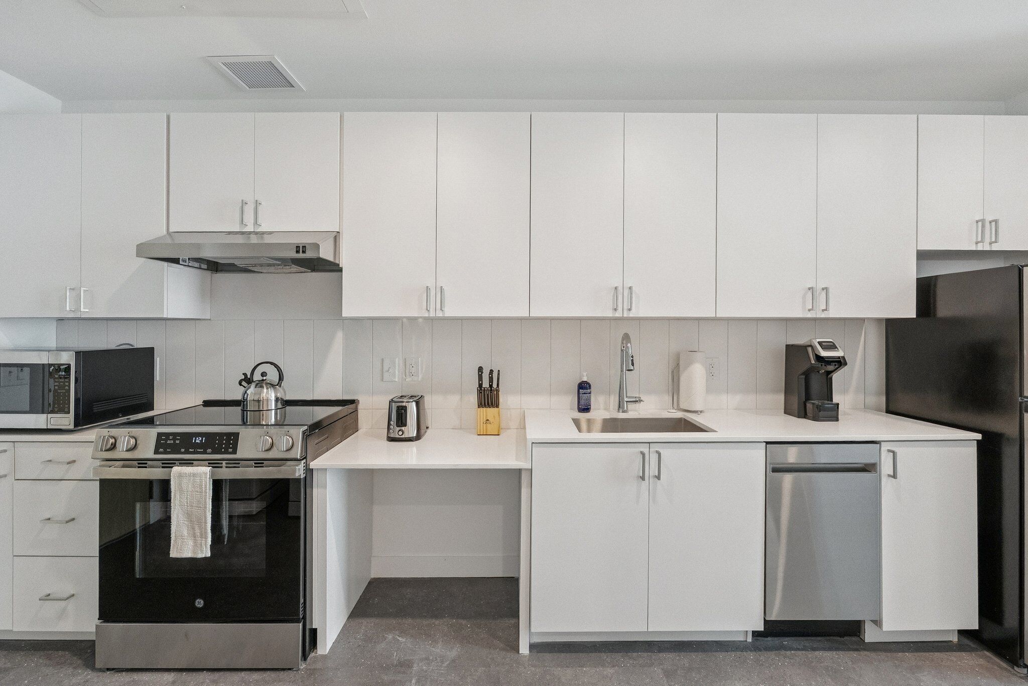 A modern kitchen with white cabinets, stainless steel appliances, and a microwave.