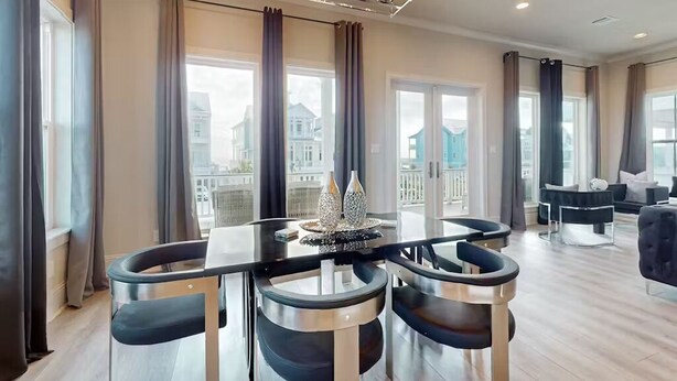 A modern living room with a dining area, large windows, and a balcony with a view of buildings. - 2nd Row Stunner w/ Gulf Views, Steps to the Beach! (Galveston)