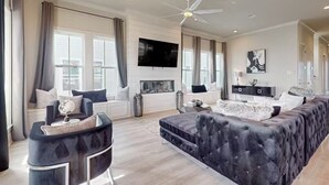 A modern living room with a large sectional sofa, a flat-screen TV mounted on the wall, and a ceiling fan. - 2nd Row Stunner w/ Gulf Views, Steps to the Beach! (Galveston)