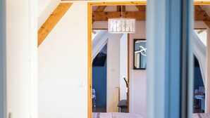 A bedroom with a sloped ceiling, wooden beams, a bed with patterned bedding, and a hanging light fixture.