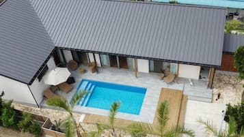 Una casa moderna con piscina, mobiliario exterior y un porche cubierto.