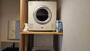 A compact laundry area with a front-loading washing machine, a dryer, and a shelf with cleaning supplies. - Private Villa isola (Tokunoshima)