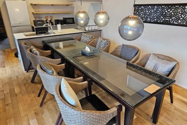 A modern kitchen with a central island, a dining area with wicker chairs, and pendant lighting.