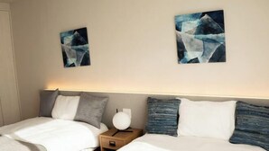 A hotel room with two beds, a nightstand, and abstract wall art. - Private Villa isola (Tokunoshima)