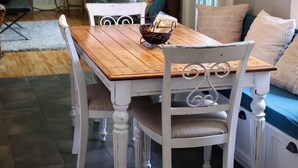 Ein Essbereich mit Holztisch und weißen Stühlen, einem Chandelier und Blick auf das Wohnzimmer.