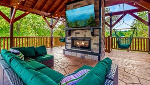 Eine Terrasss mit Kamin aus Stein, grünen Sitzpolstern und einer Hängematte.