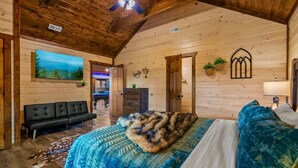 Ein gemütliches Schlafzimmer in einer Blockhütte mit einem Bett, einer schwarzen Couch und einem Bild an der Wand.