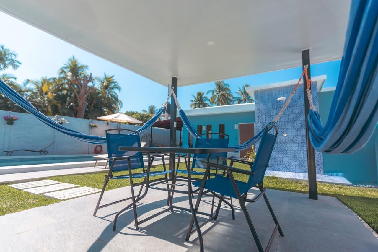Zona de piscina con sillas azules y una mesa, una hamaca y una pared azul con diseño de azulejos.