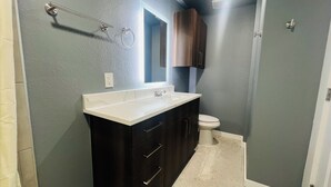 Un baño con lavamanos blanco, muebles oscuros, un espejo y un inodoro.