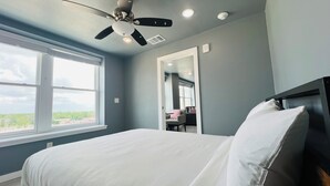 Un dormitorio con cama, ventilador de techo, ventana y puerta que da a otra habitación.