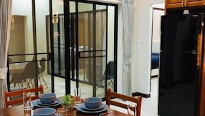 Un tavolo da pranzo apparecchiato con piatti e bicchieri azzurri, un frigorifero nero e una porta vetrata scorrevole che dà su uno spazio esterno.