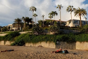 A beach with palm trees, a stone wall, and a building in the background. - The Pool House Pattaya No.8 (Pattaya)