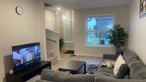 A living room with a TV, sofa, coffee table, and a staircase leading to an upper level. - Cozy quiet place 15 min driver to airport perfect place for family and friends. (Calgary)